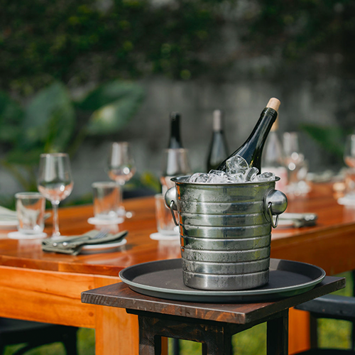 Mesa lista con copas y platos y una champagnera con botella de vino