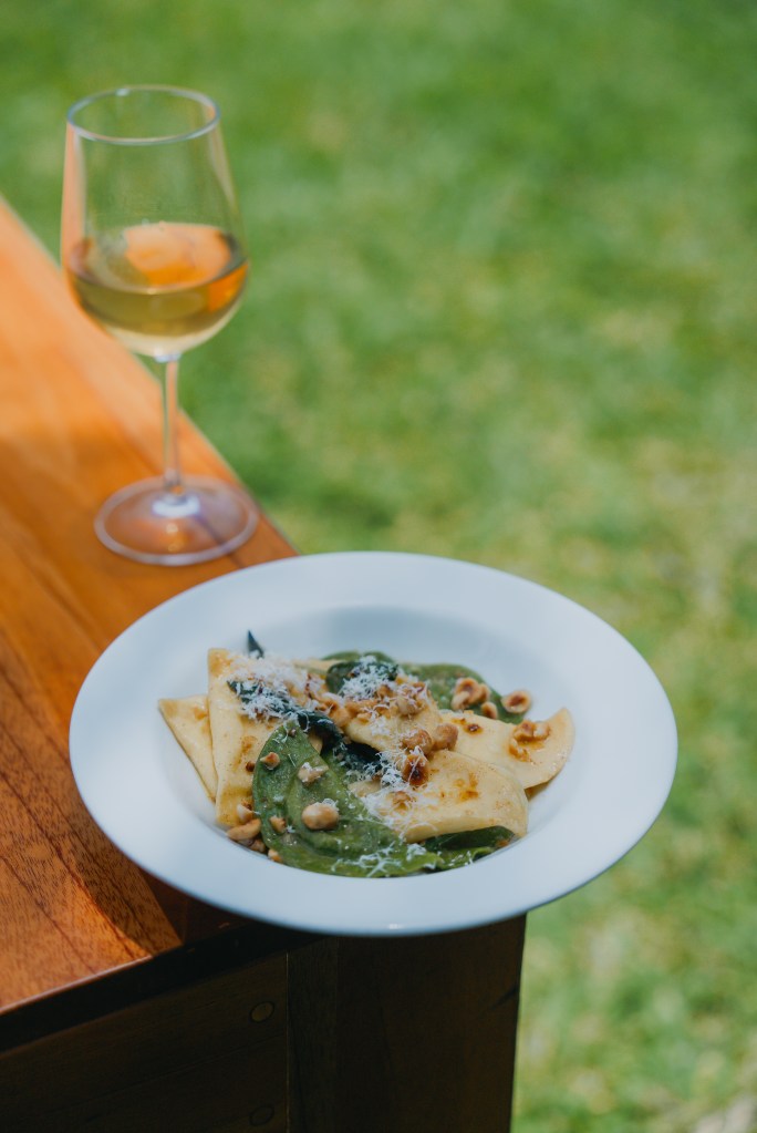 plato de pasta en la esquina de una mesa en el jardín con una copa de vino blanco